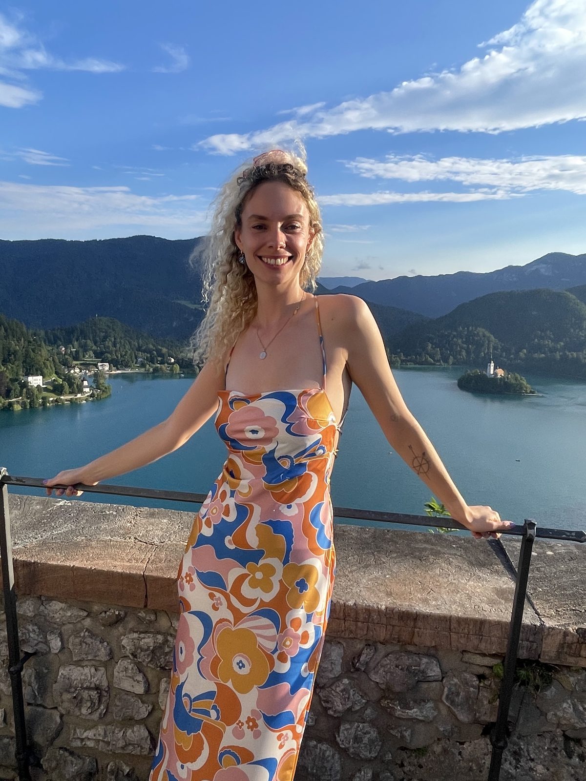 Shann smiling in bright sunlight, a lake and wooded hills behind her